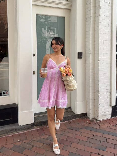 Woman in a pink striped dress standing on a sidewalk in front of a building