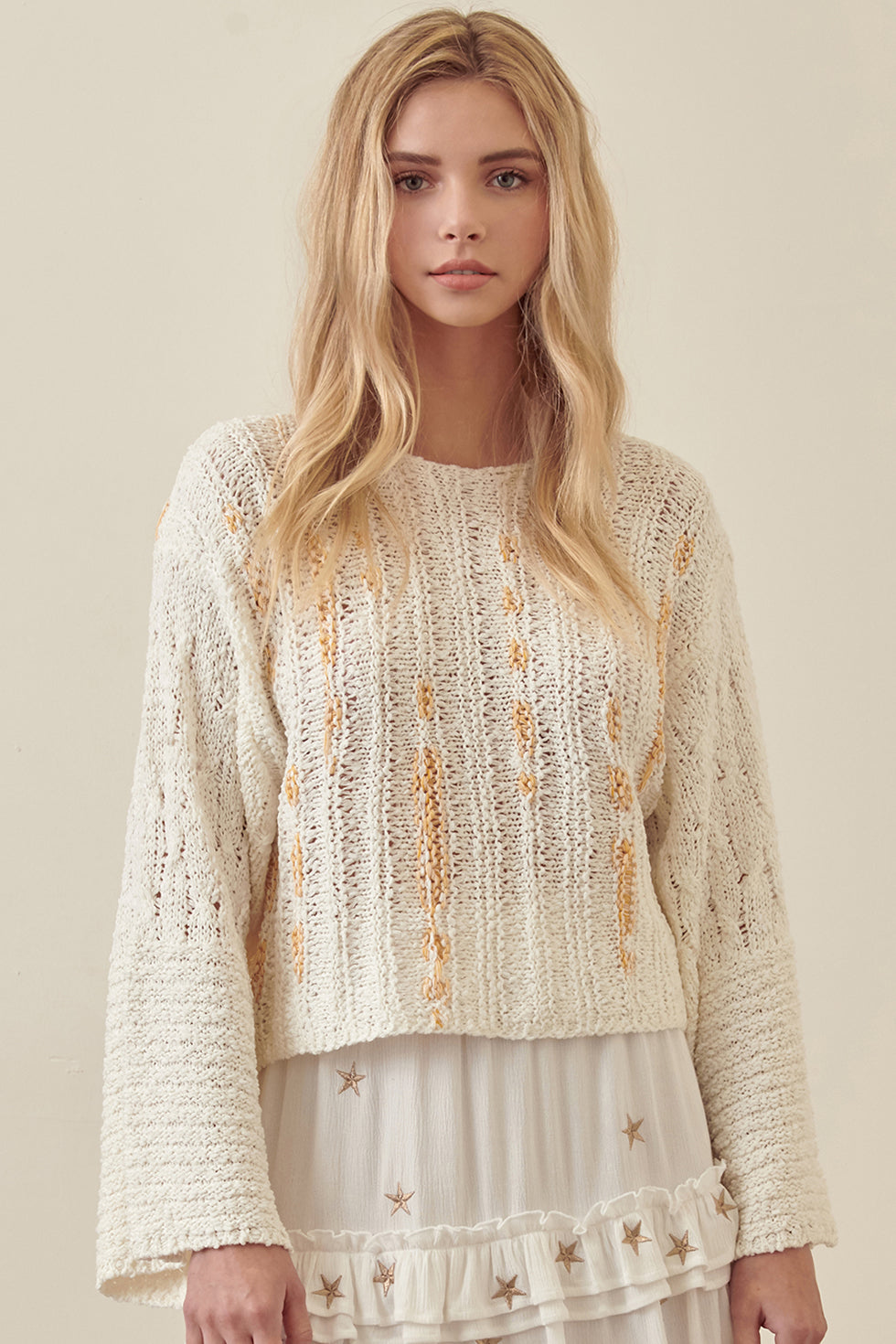 Woman wearing a cream-colored knitted sweater with floral patterns on a beige background