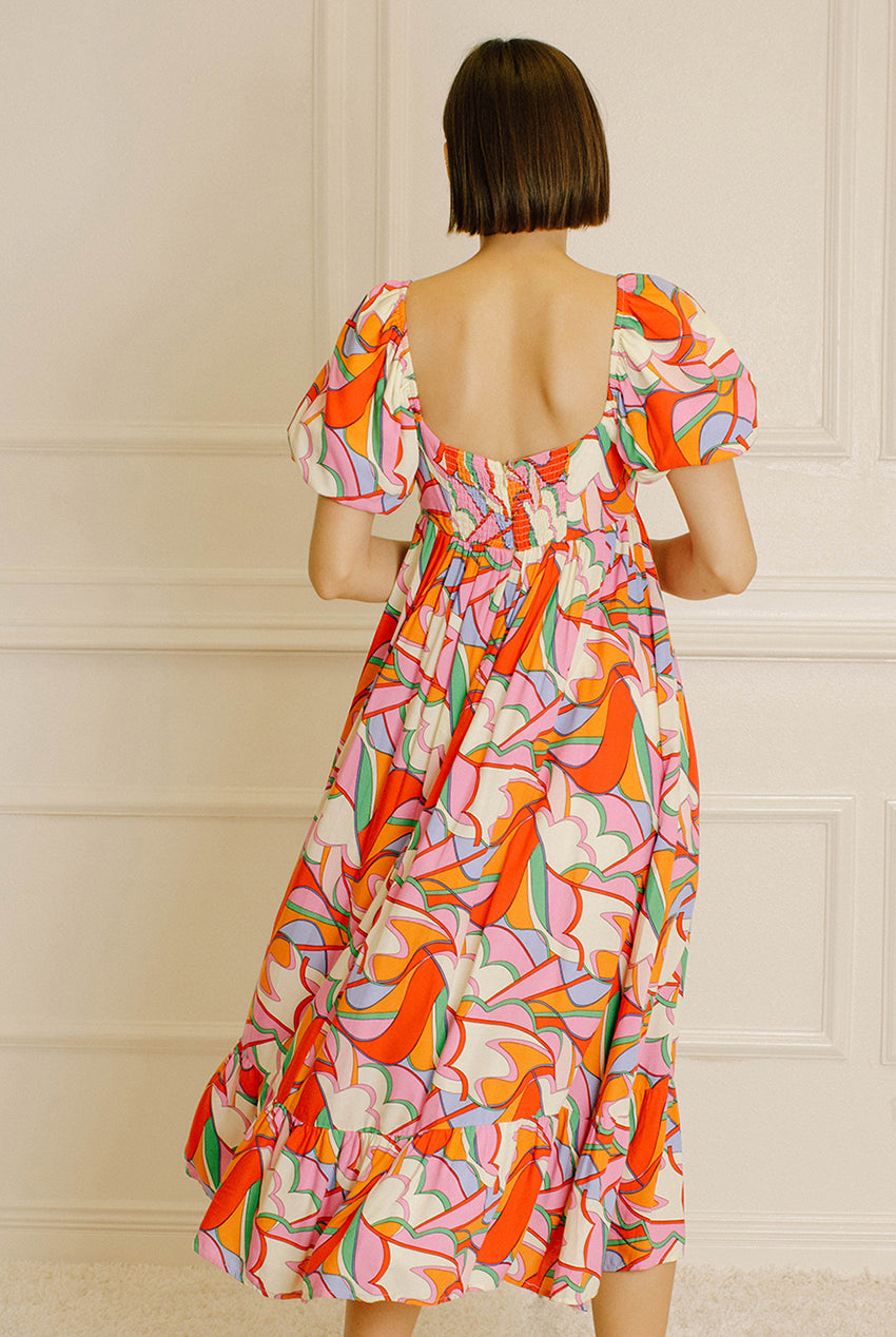 Back view of a woman wearing a colorful patterned dress against a neutral wall.