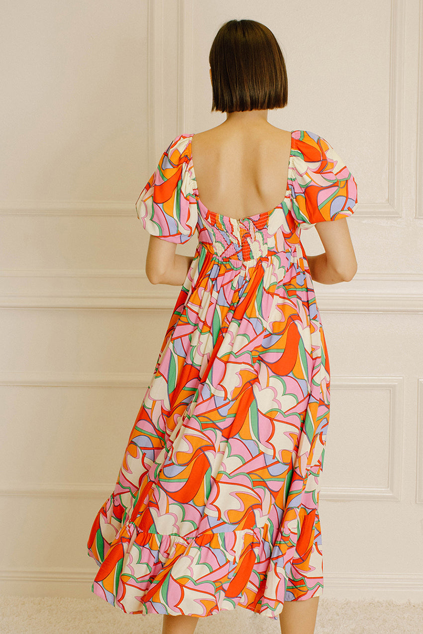 Back view of a woman wearing a colorful patterned dress against a neutral wall.