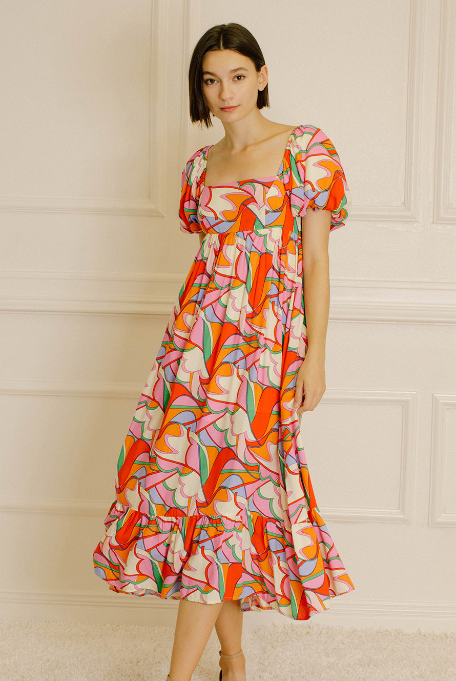 Woman wearing a colorful patterned dress against a neutral wall.
