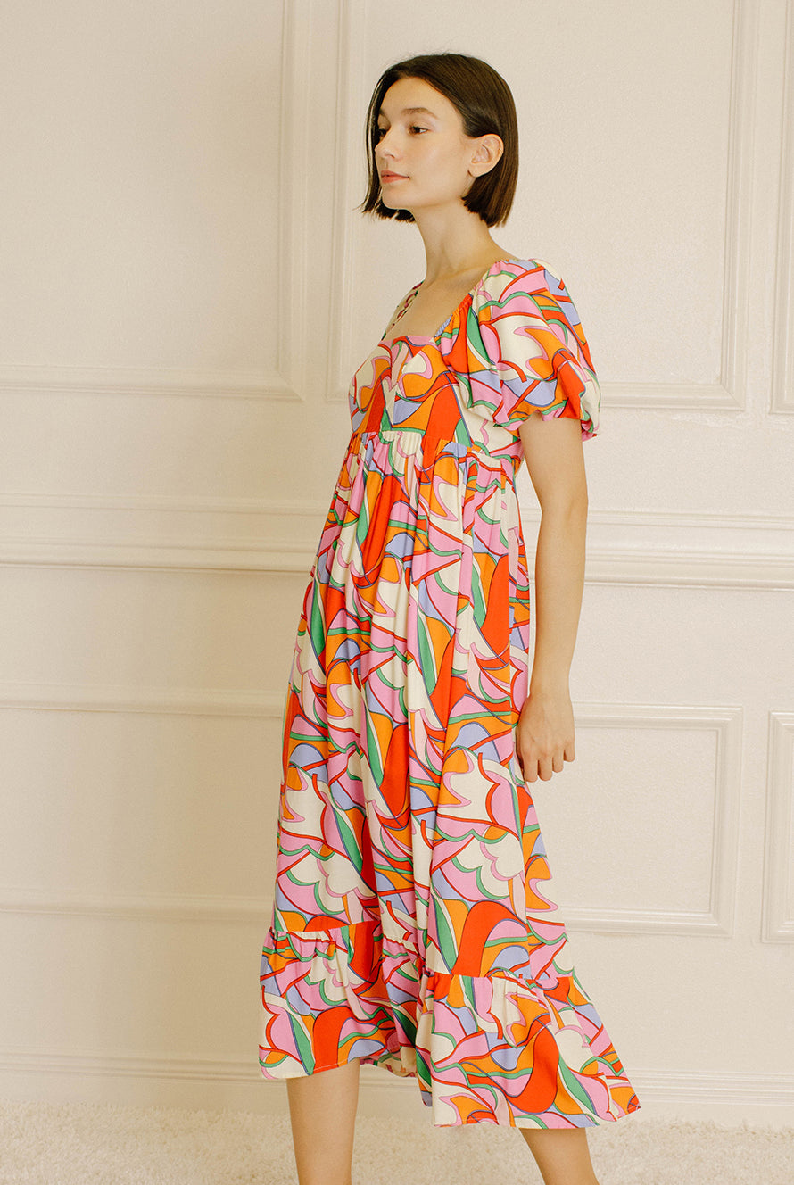 Side view of a woman wearing a colorful patterned dress against a neutral wall.