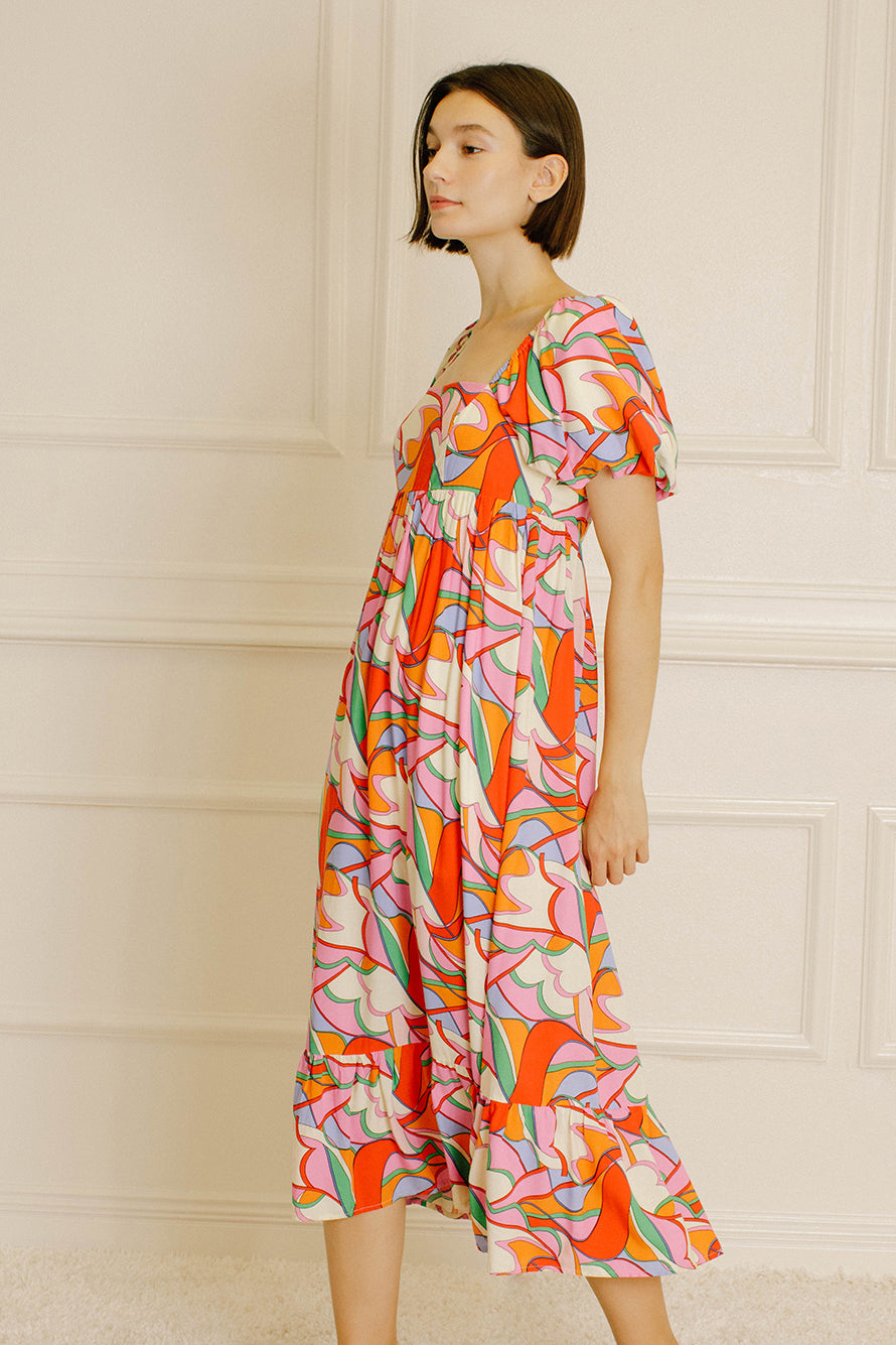 Side view of a woman wearing a colorful patterned dress against a neutral wall.