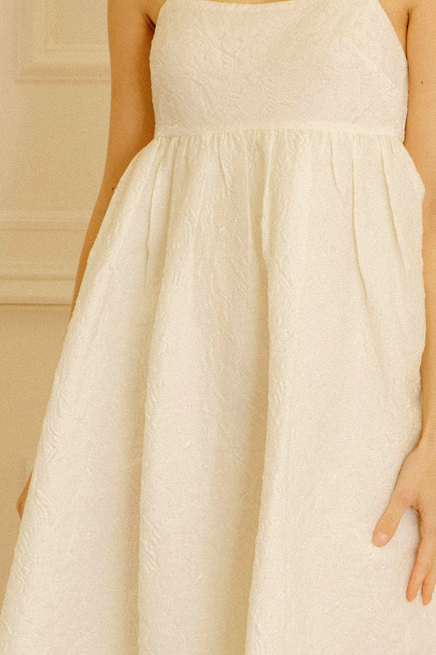 A cream dress with floral jacquard details against a light-colored wall