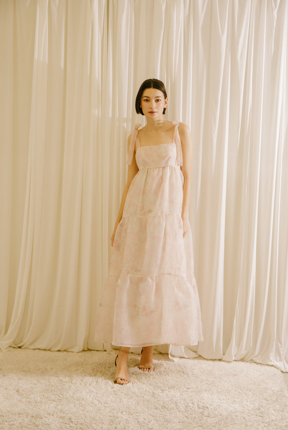 Woman in a light pink dress standing against a white curtain backdrop