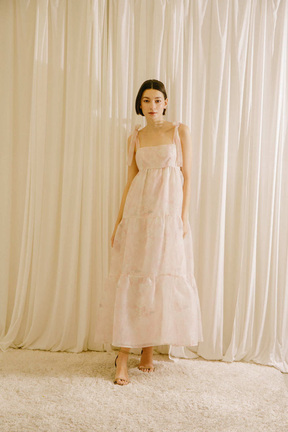 Woman in a light pink dress standing against a white curtain backdrop