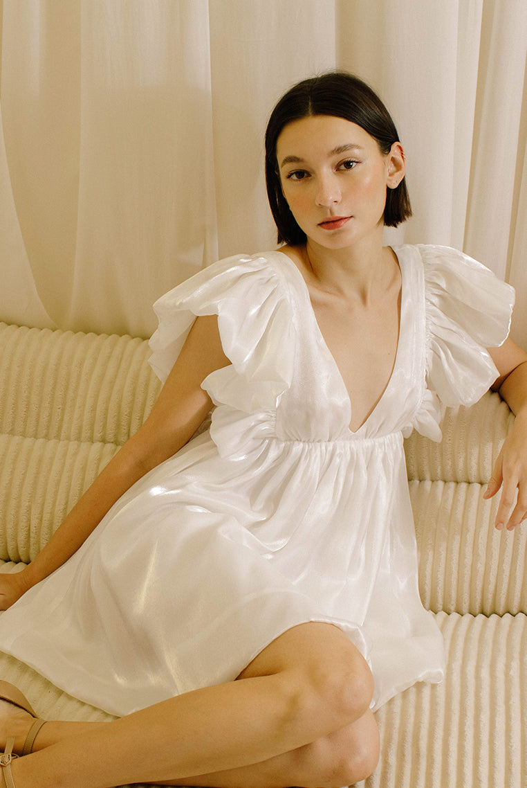 Woman in a white dress with a v-neckline sitting on a beige sofa with a neutral background
