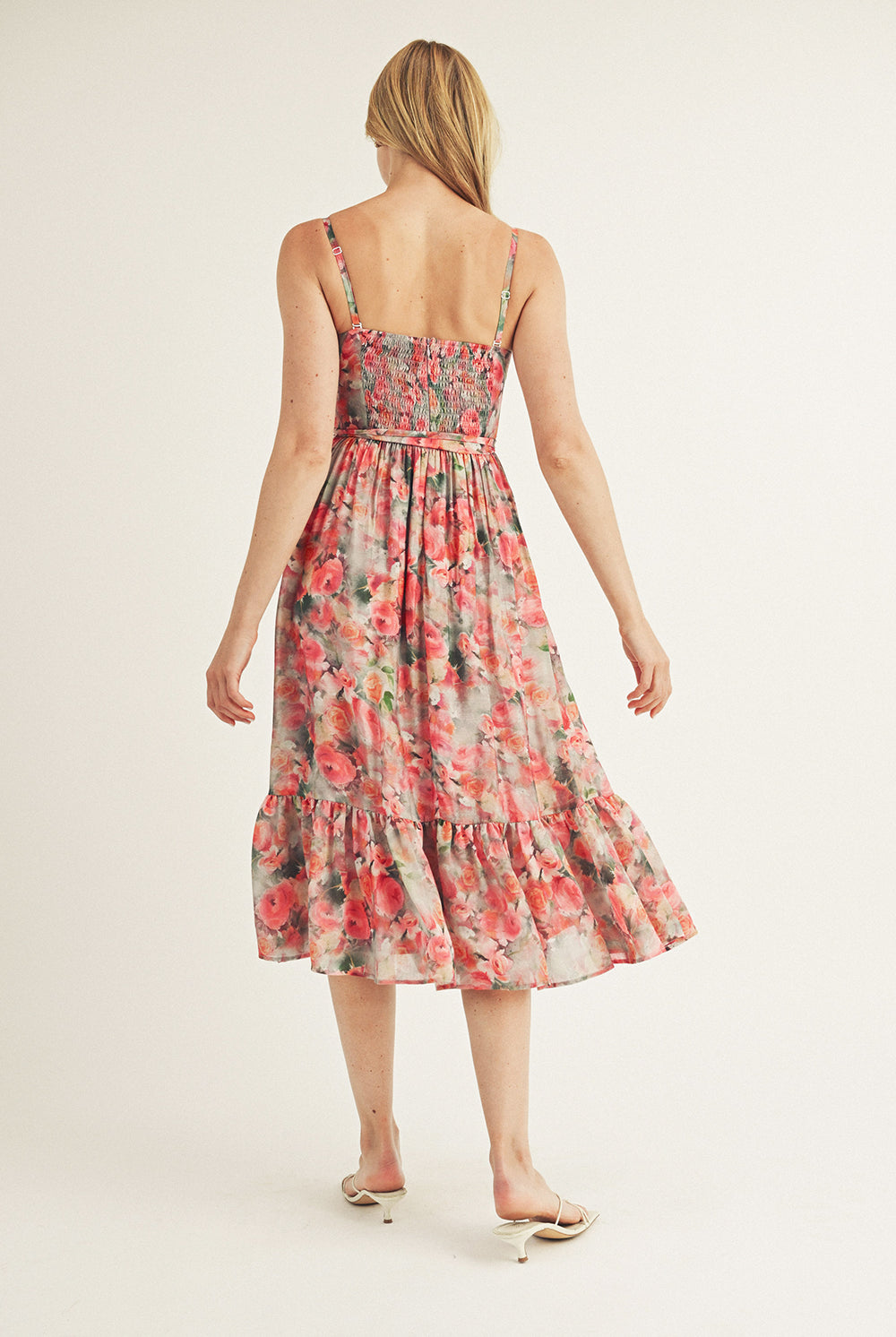 Back view of a woman wearing a pink watercolor rose print midi dress with a sweetheart neckline and ruffled hem.