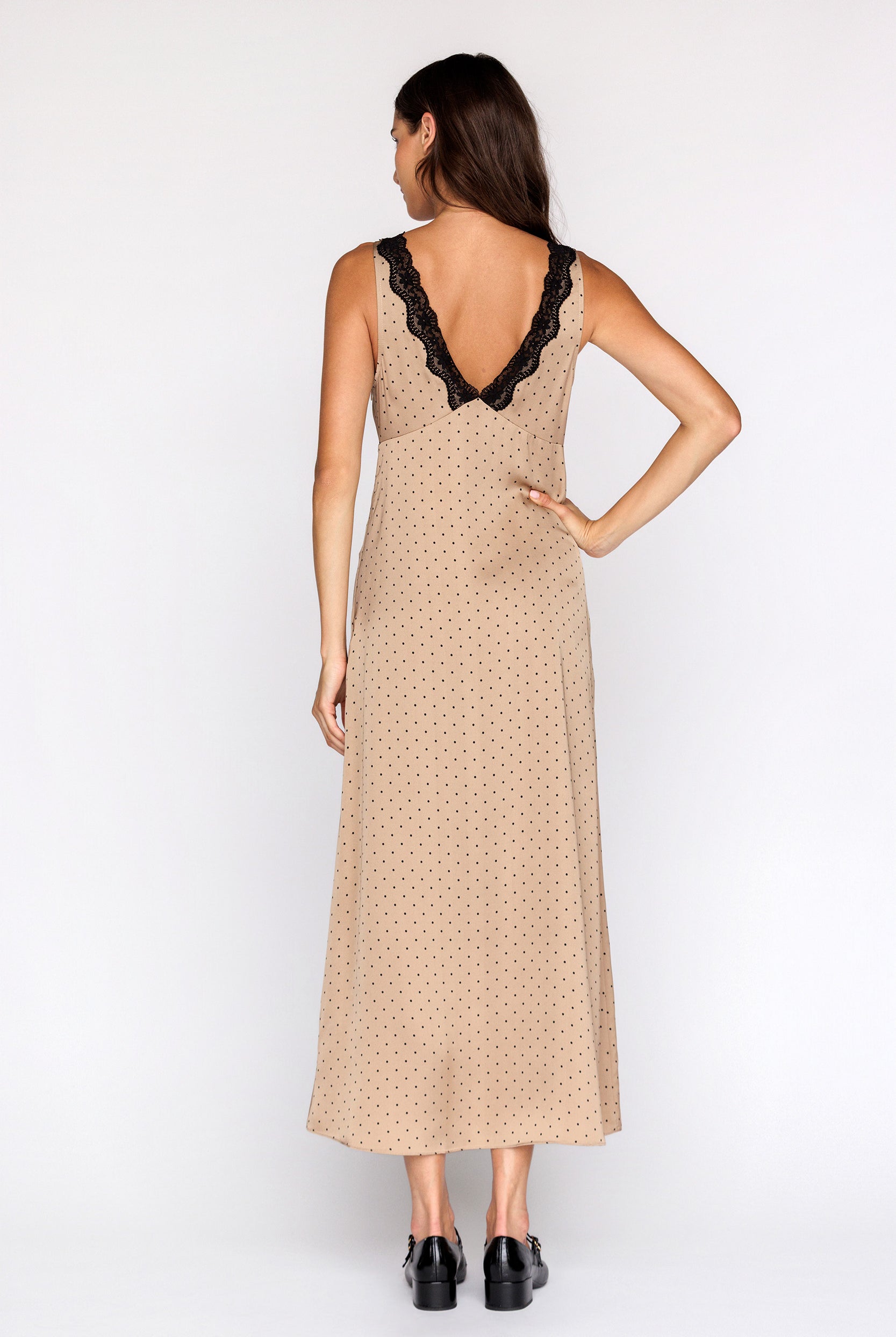 Woman wearing a bronze with black polka dot dress with black lace details on a white background