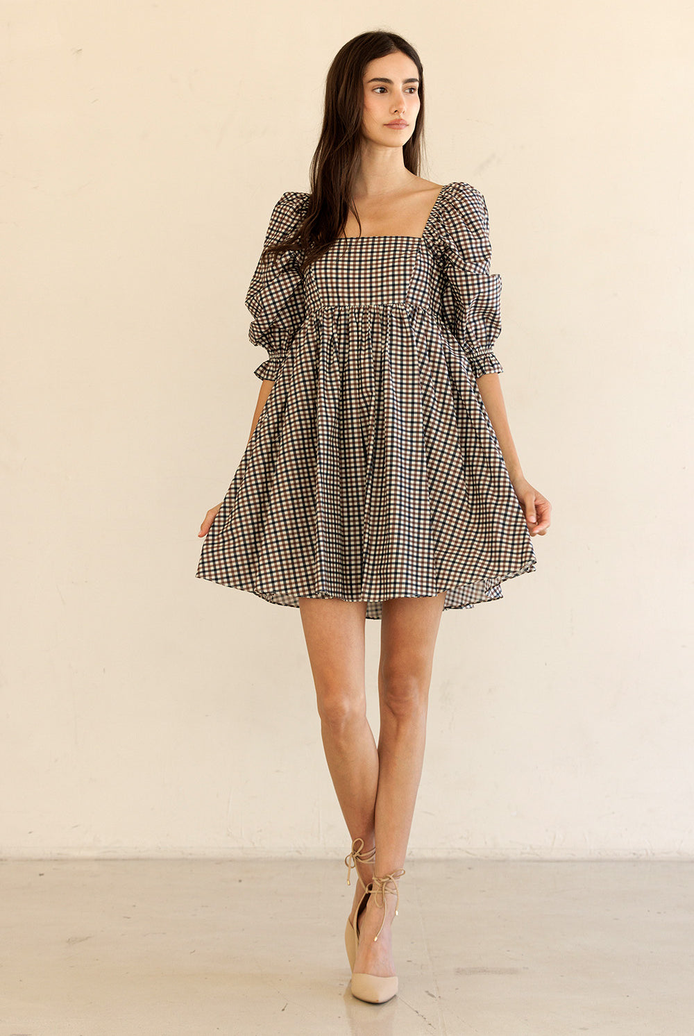 Woman wearing a checkered dress with puff sleeves and beige heels against a plain background