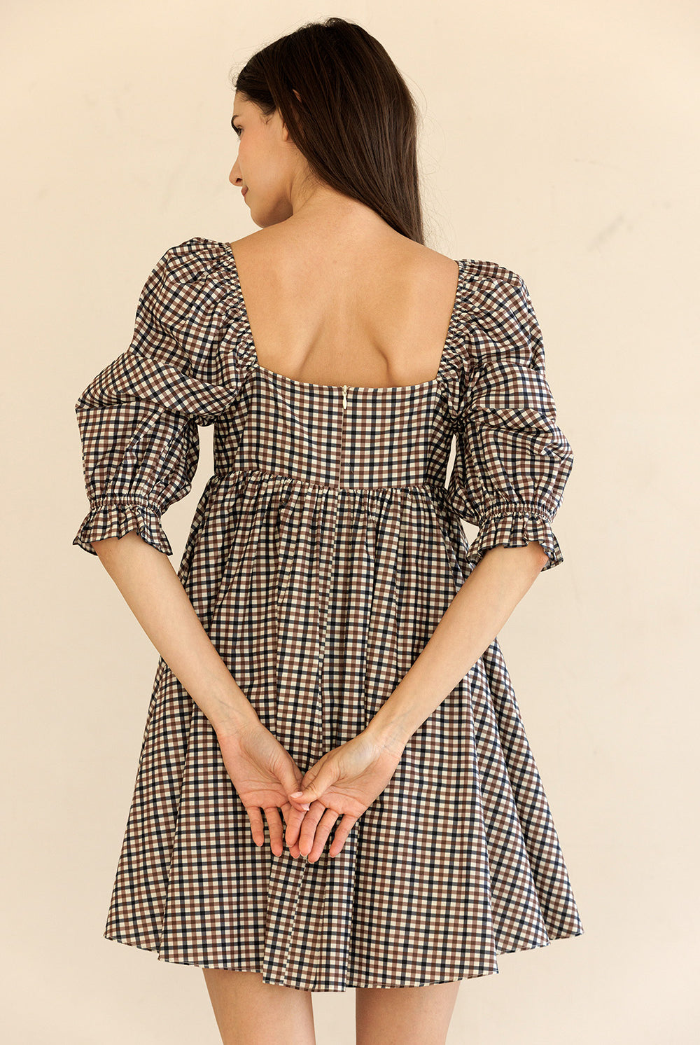 Woman wearing a brown checkered dress with puff sleeves on a beige background