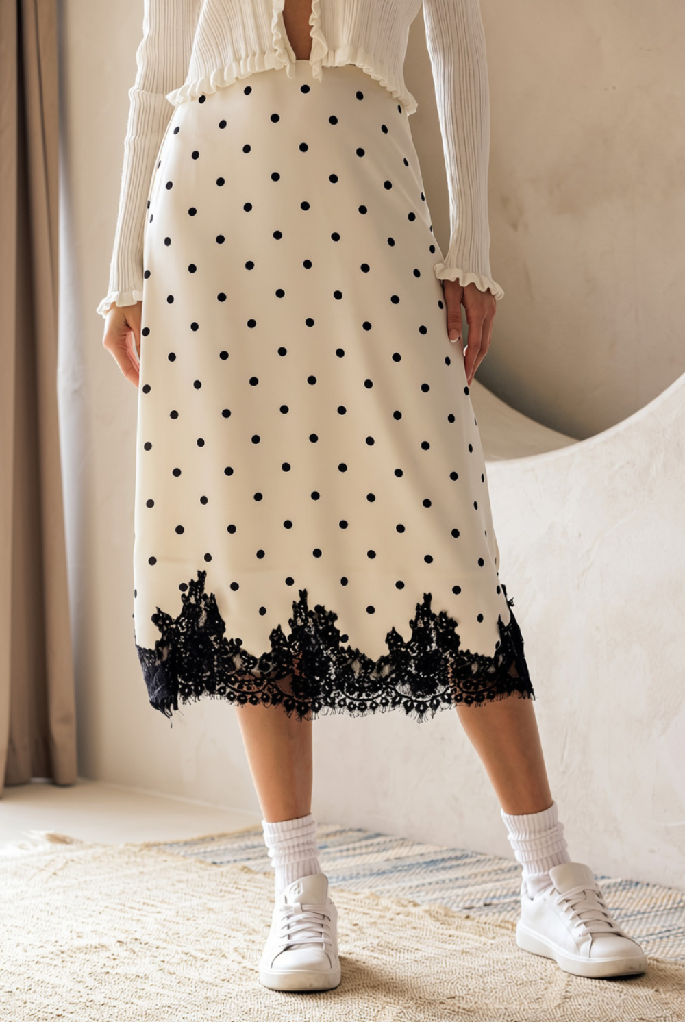 A person wearing a midi skirt that features an ivory and black polka dot print, A-line silhouette and a black lace-trimmed hem.