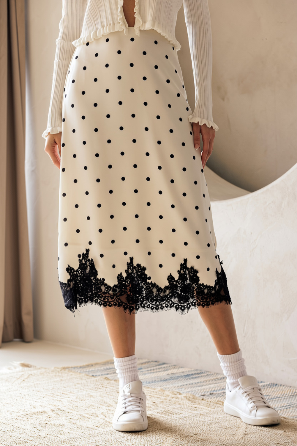 A person wearing a midi skirt that features an ivory and black polka dot print, A-line silhouette and a black lace-trimmed hem.