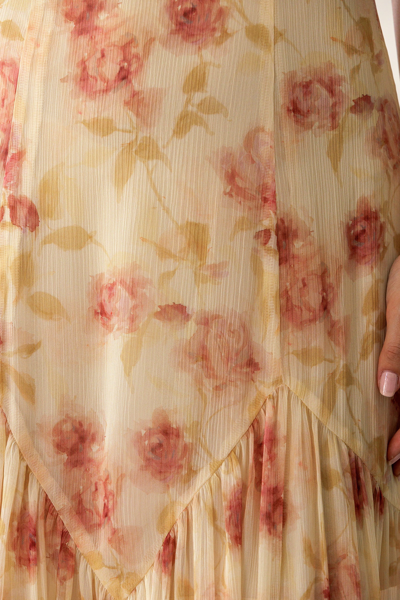 Close-up of a sheer cream-colored fabric with a pink and beige floral print, featuring a ruffled hem and a hand holding the side.