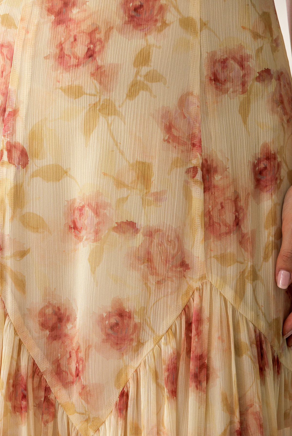 Close-up of a sheer cream-colored fabric with a pink and beige floral print, featuring a ruffled hem and a hand holding the side.