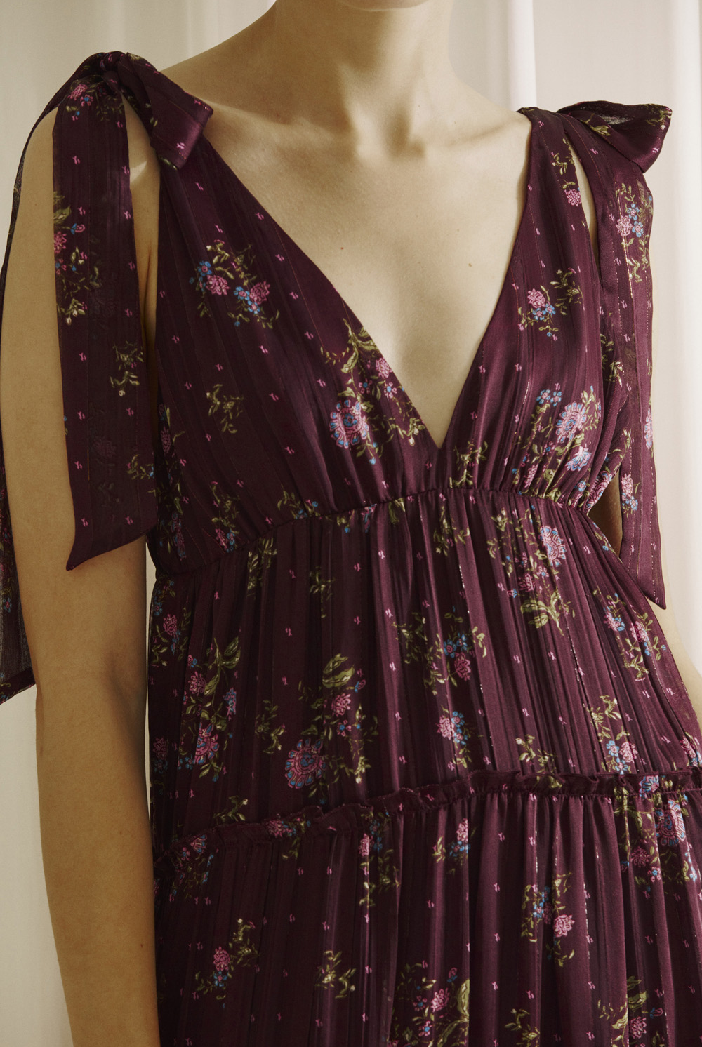 Close-up of a person wearing a plum base with an allover pink floral print dress with a deep v-neckline in a white background