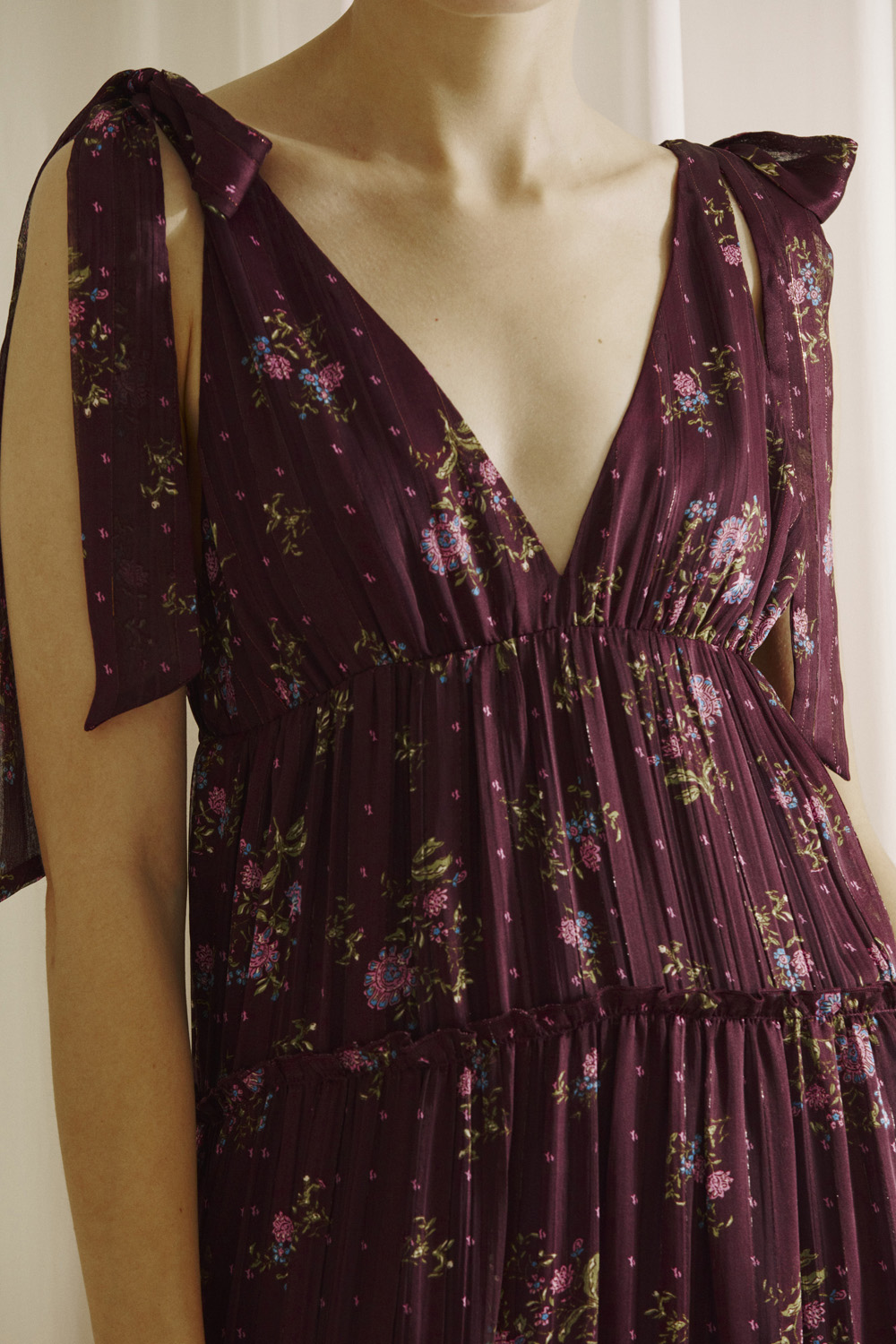 Close-up of a person wearing a plum base with an allover pink floral print dress with a deep v-neckline in a white background