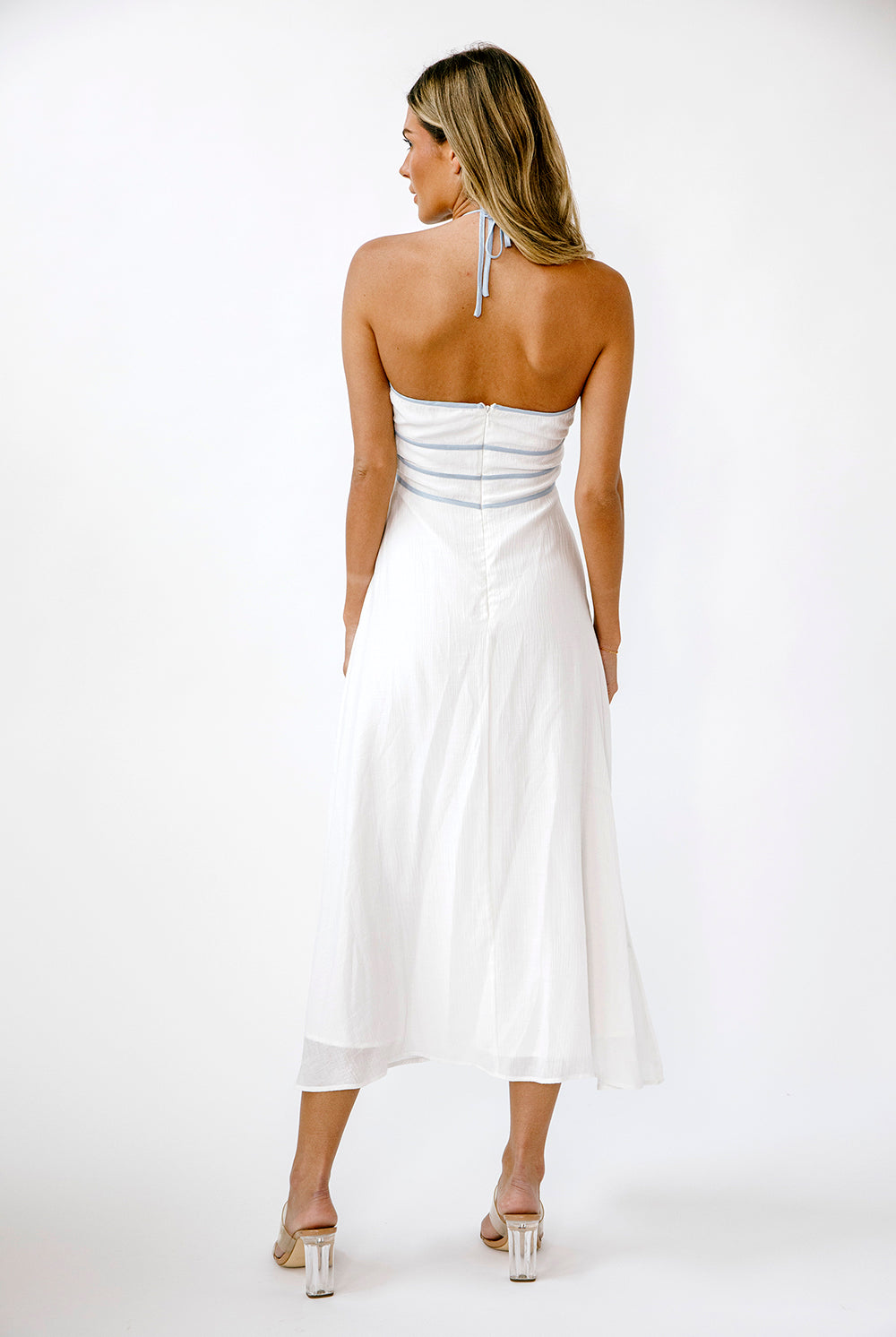 Back view of a woman wearing a white dress with blue accents on a white background