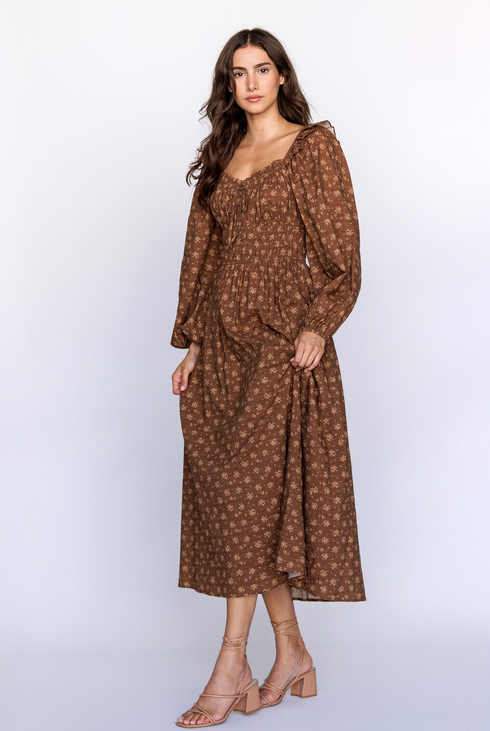 Woman wearing a brown patterned dress and beige heels on a white background