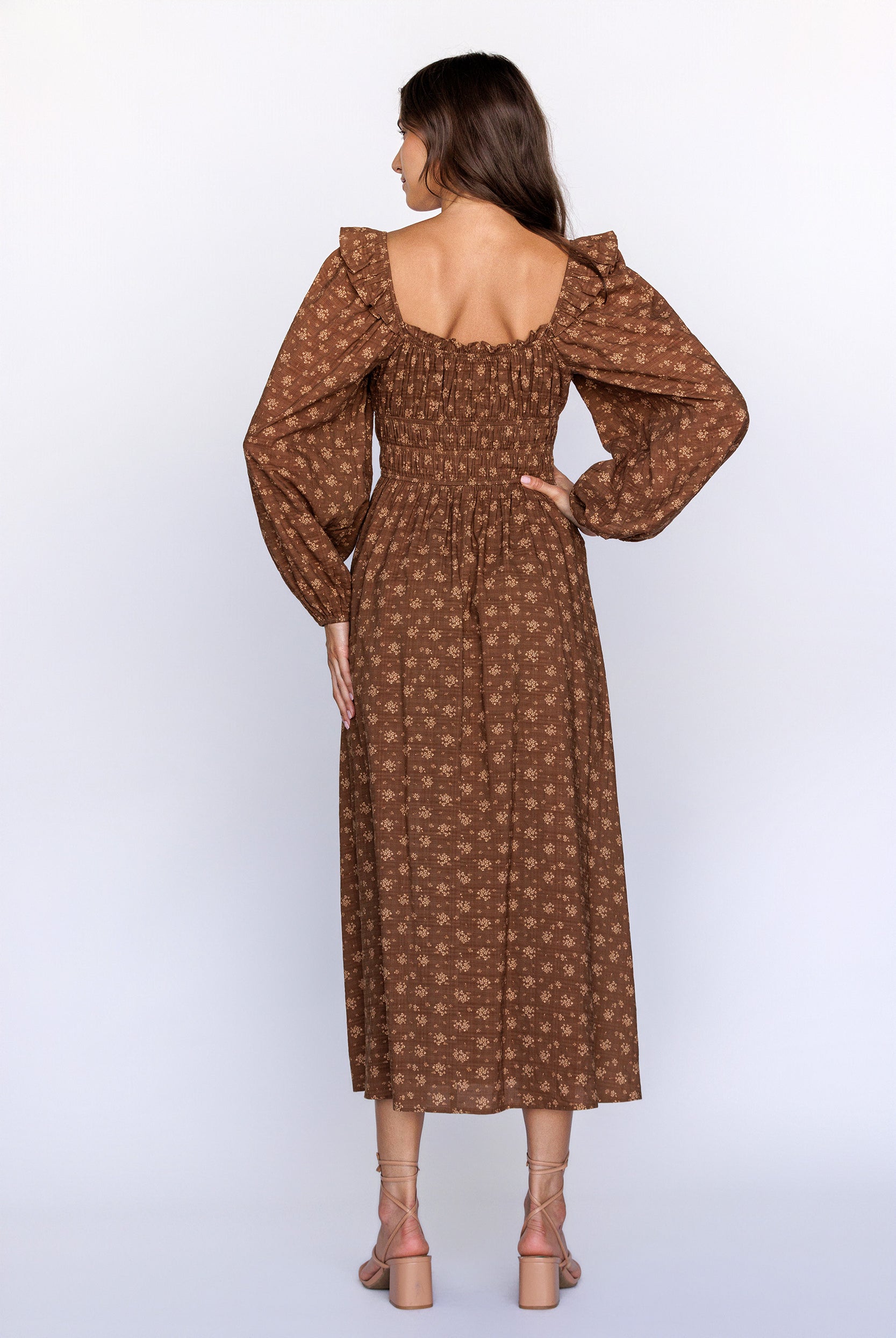 Back view of a woman wearing a brown patterned dress with long sleeves on a white background