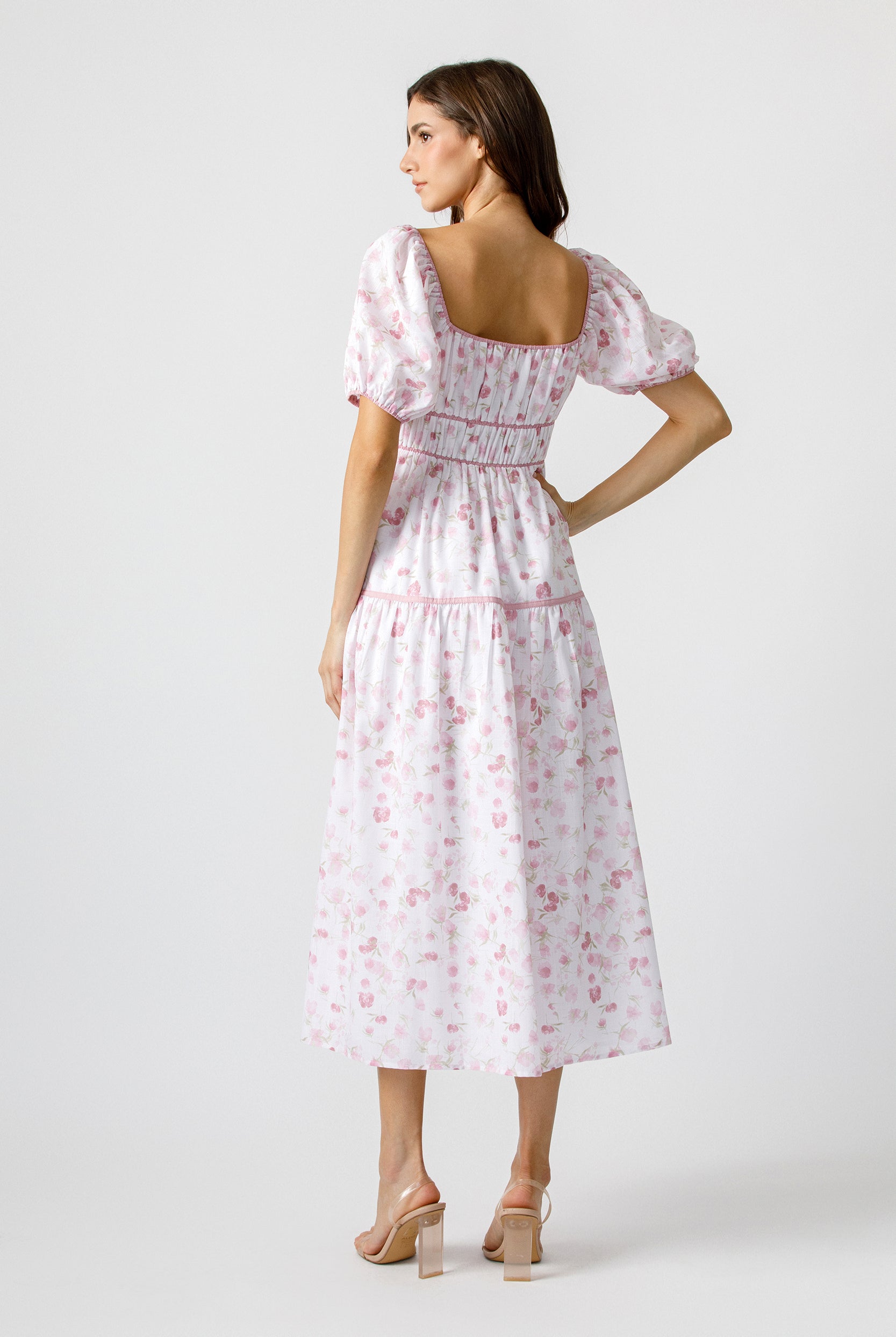 Back view of woman wearing a white dress with pink floral pattern on a white background