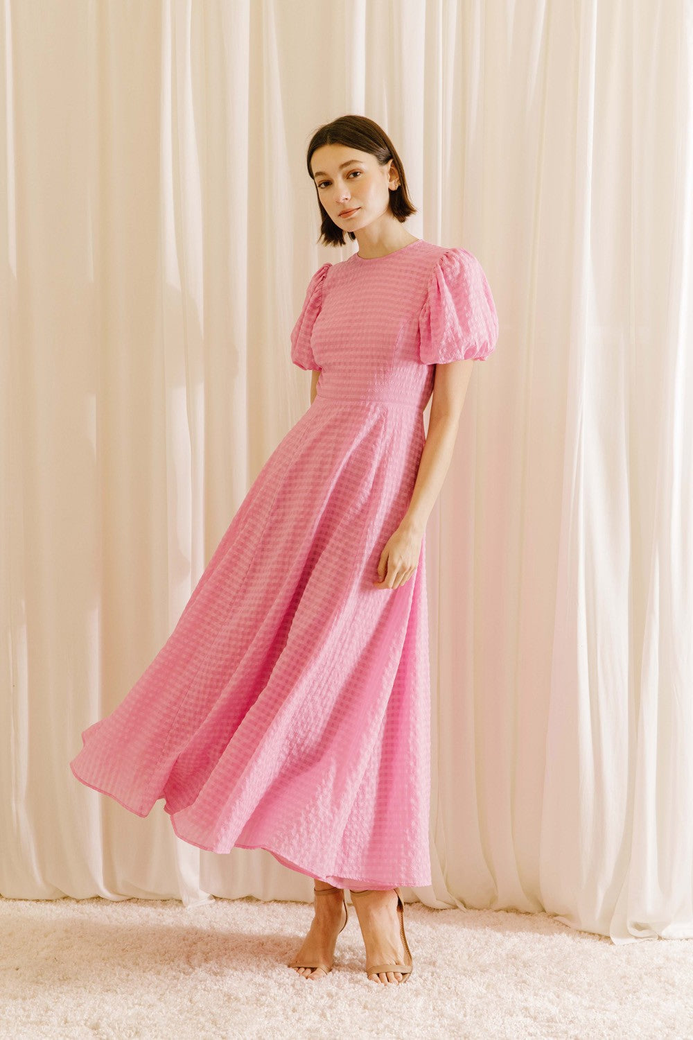Woman wearing a pink dress against a beige curtain background