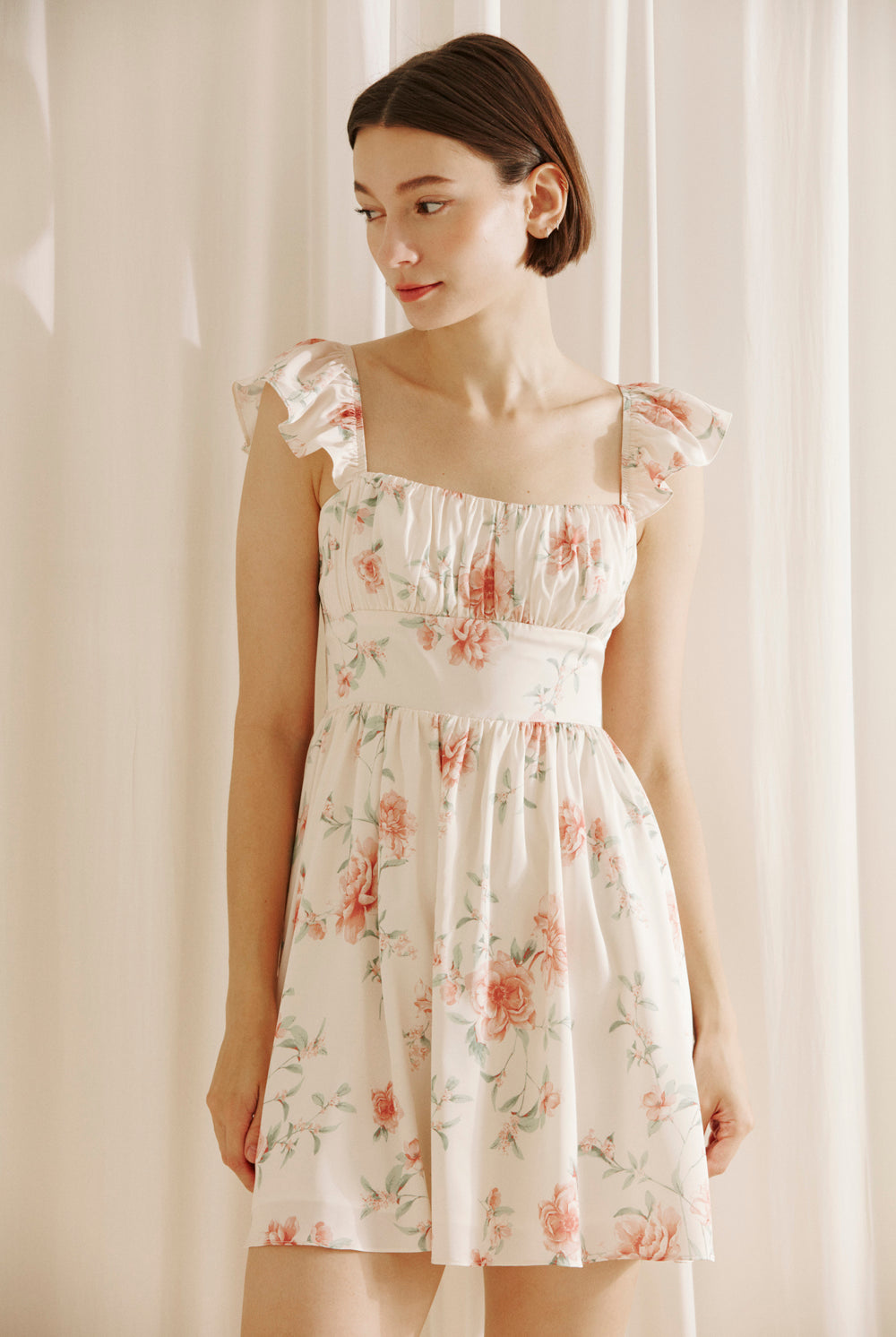 Woman wearing a cream floral mini dress against a plain background