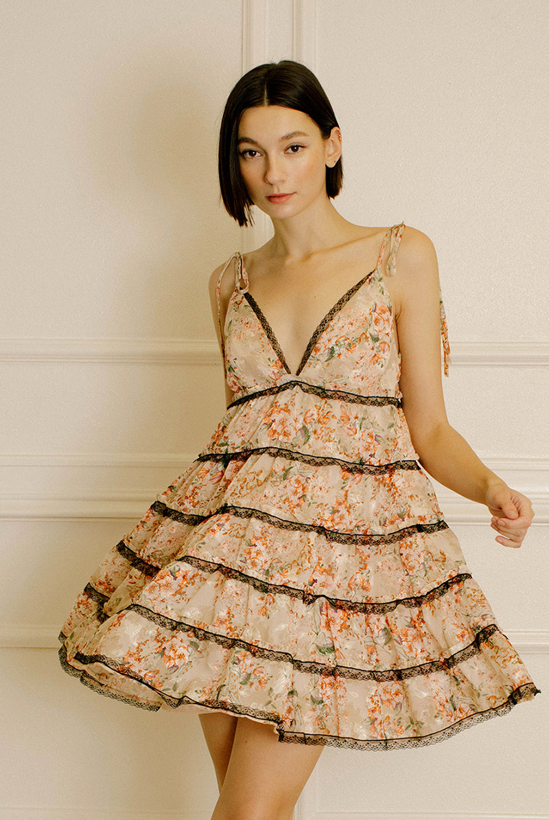 Woman wearing a peach floral dress with lace details against a neutral wall.