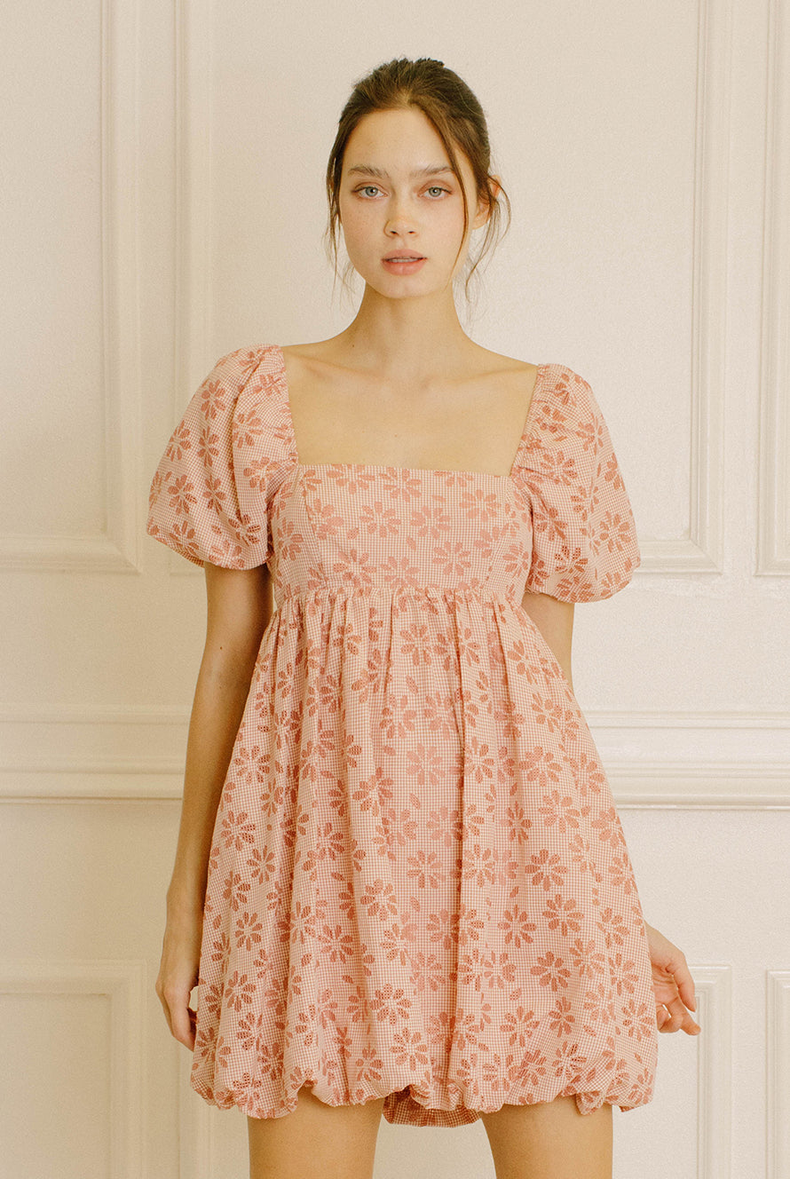 Woman wearing a pink gingham with floral embroidery mini dress against a neutral background