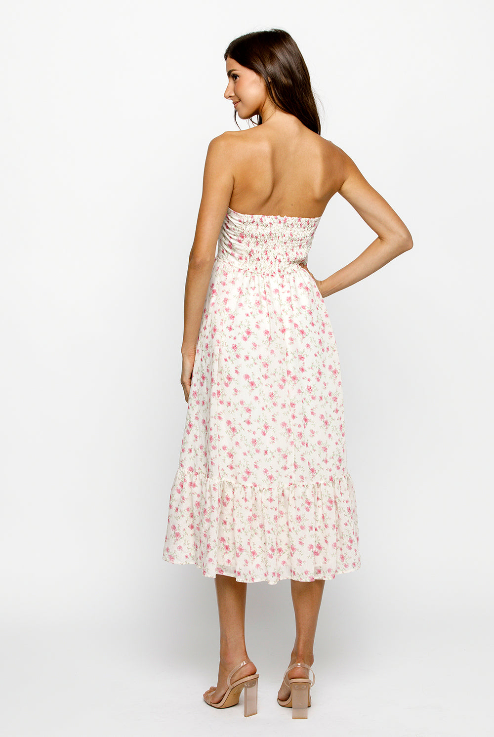 Back view of a woman wearing a strapless cream floral dress on a white background