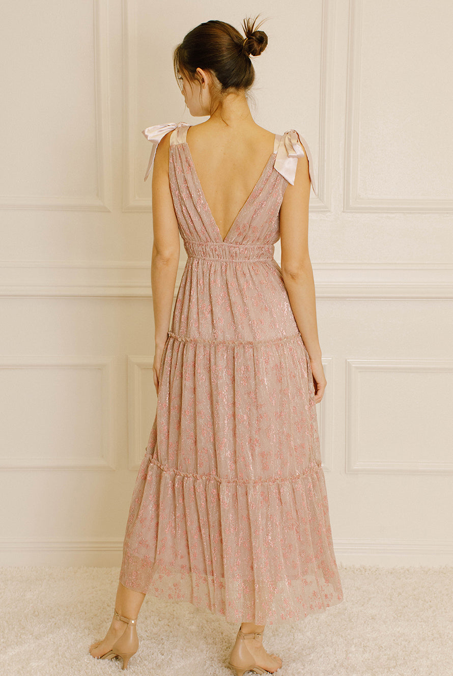 Back view of a woman wearing a pink metallic floral dress against a neutral wall.