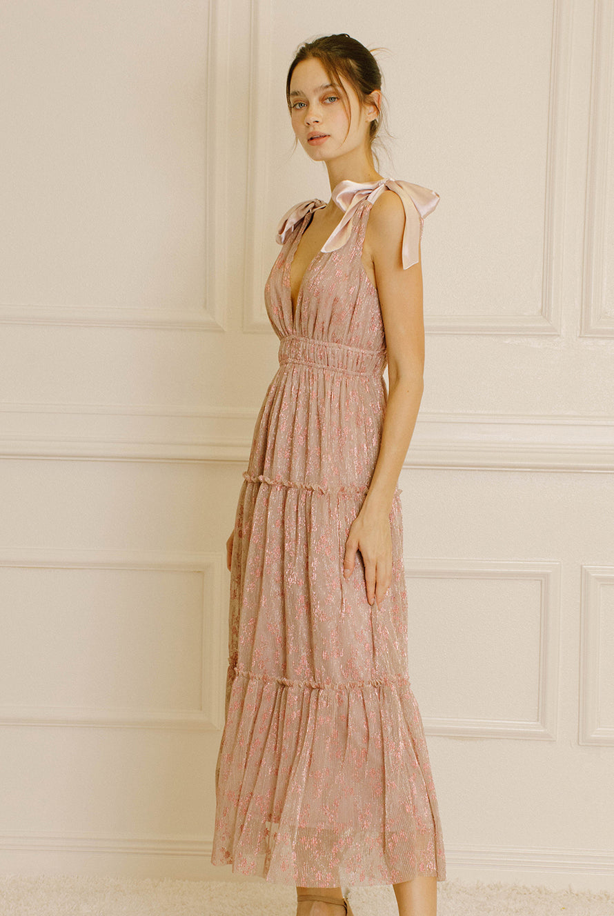 Side view of a woman wearing a pink metallic floral dress against a neutral wall.