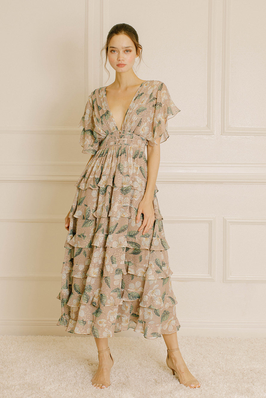 Woman wearing a beige and green floral dress in a room with white paneled walls.