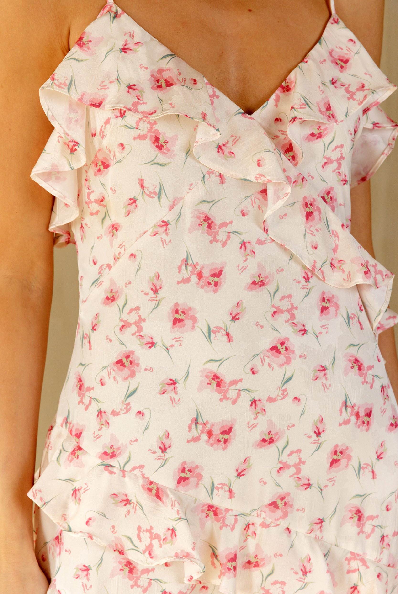A close-up of a ruffled dress with a pink floral print on a cream background, worn by a model.