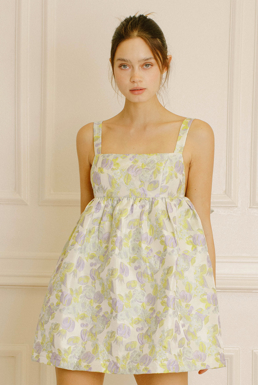 Woman wearing a green and violet dress with embroidered leave against a neutral background