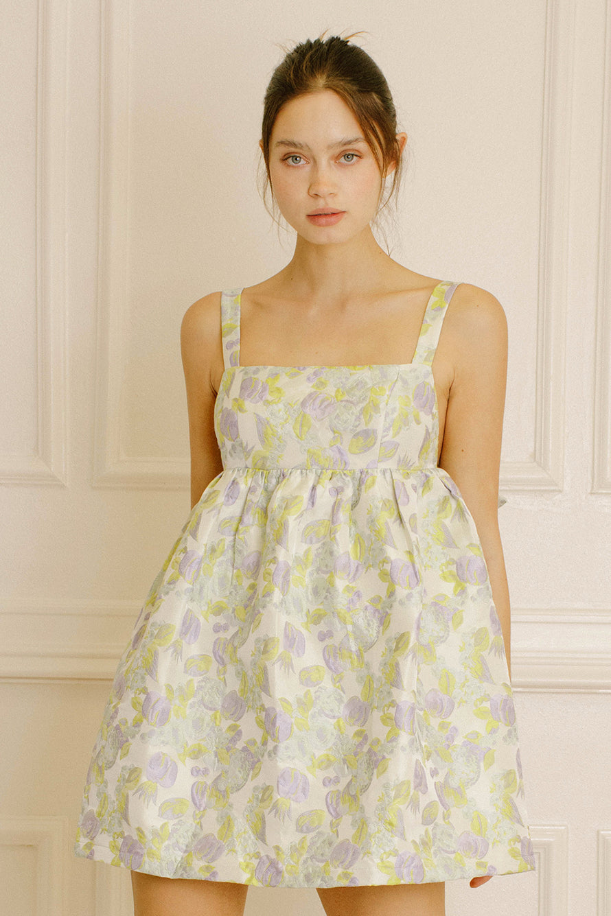 Woman wearing a green and violet dress with embroidered leave against a neutral background