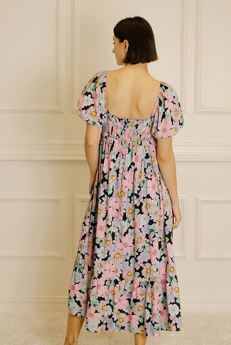 Back view of a woman wearing a pastel floral midi dress against a beige wall