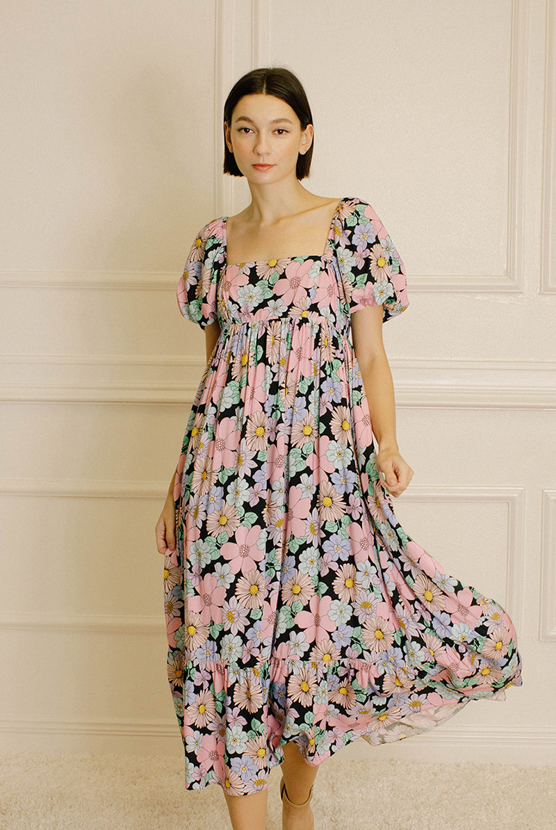 Woman wearing a pastel floral midi dress against a beige wall.