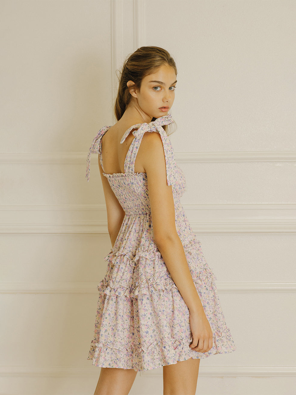 Back view of a woman wearing a floral dress with a white wall background