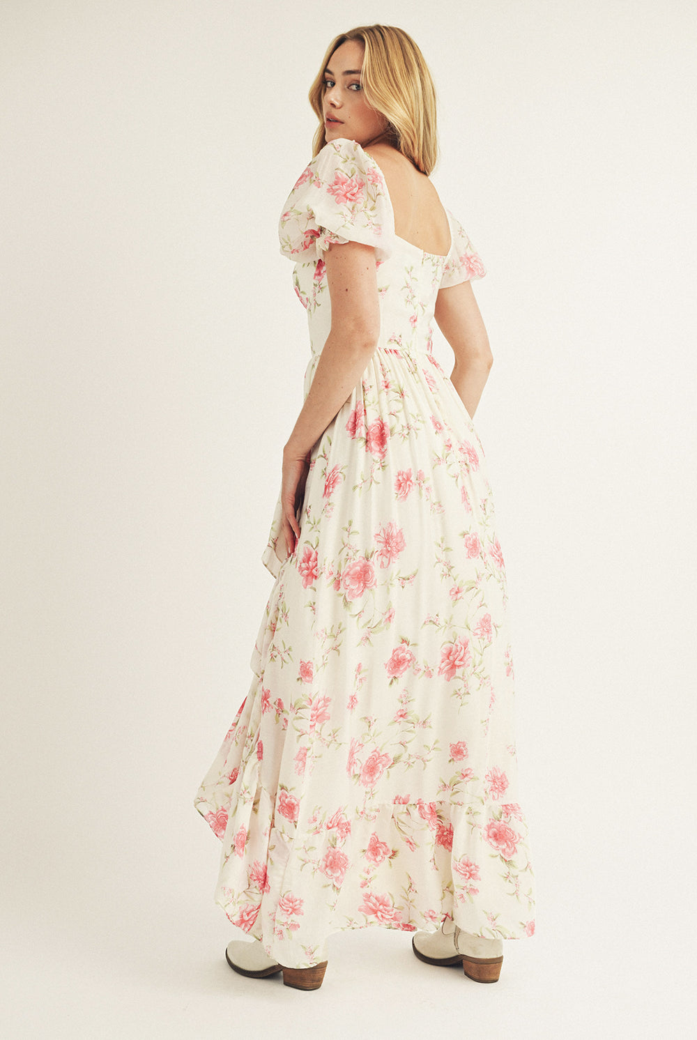 Back view of a woman wearing a floral dress and white cowboy boots on a plain background