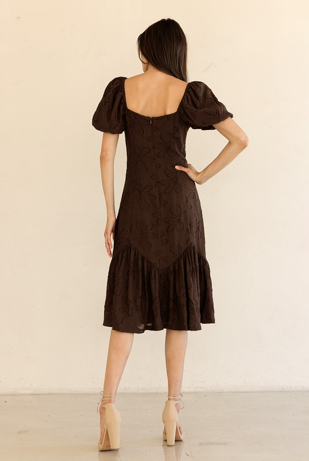 Woman wearing a brown dress with puff sleeves against a beige background