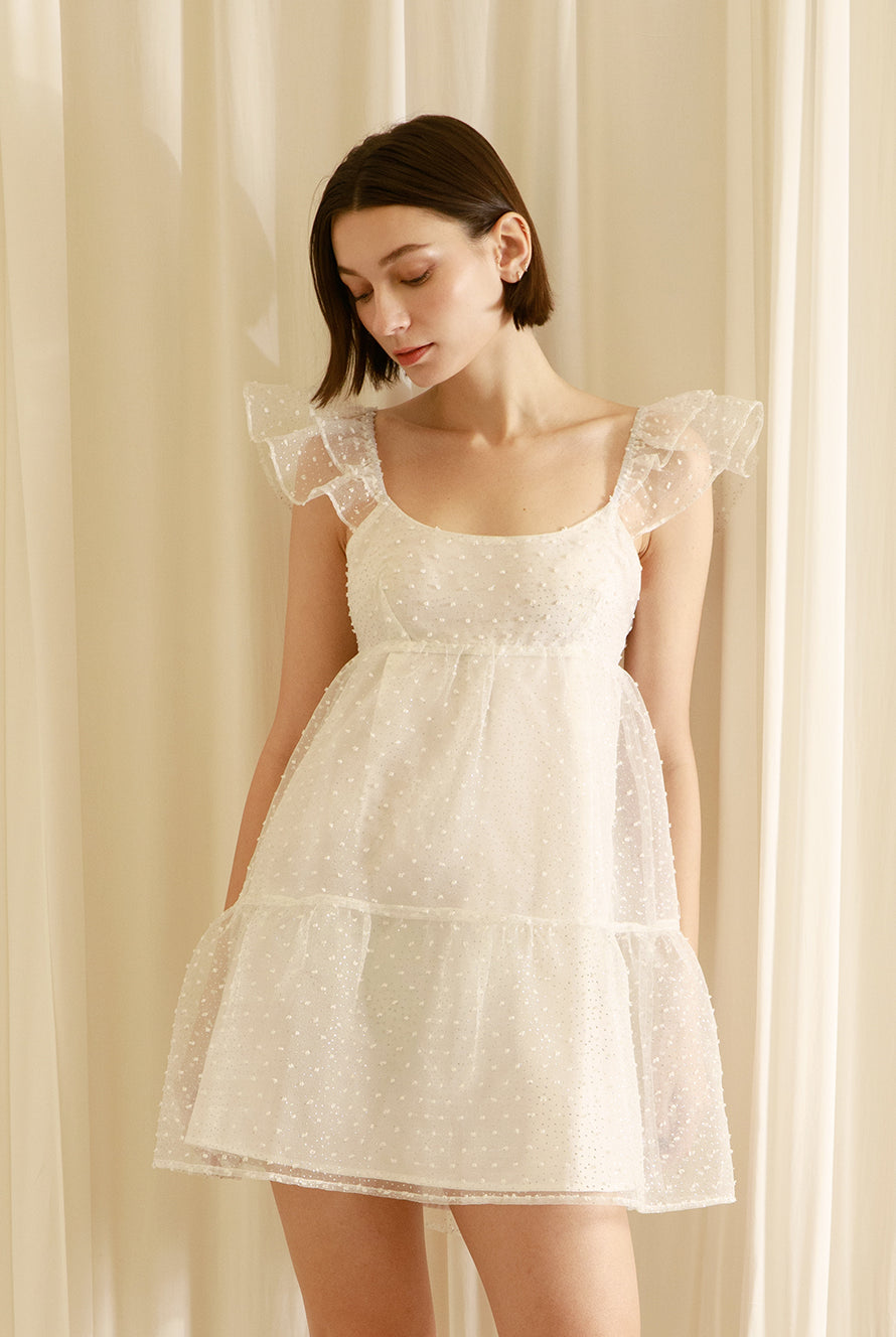 Woman wearing a white dress against a beige curtain background