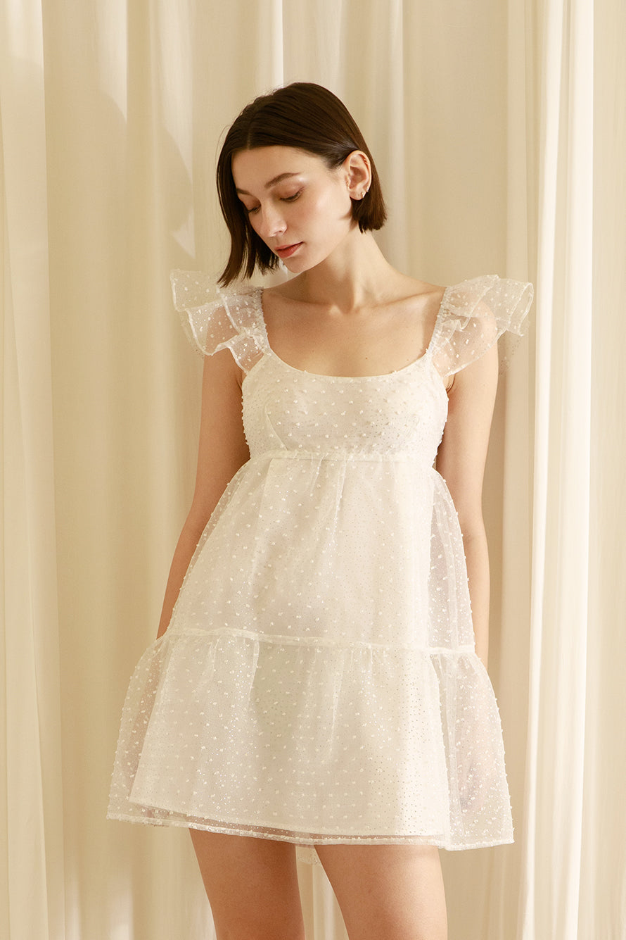 Woman wearing a white dress against a beige curtain background