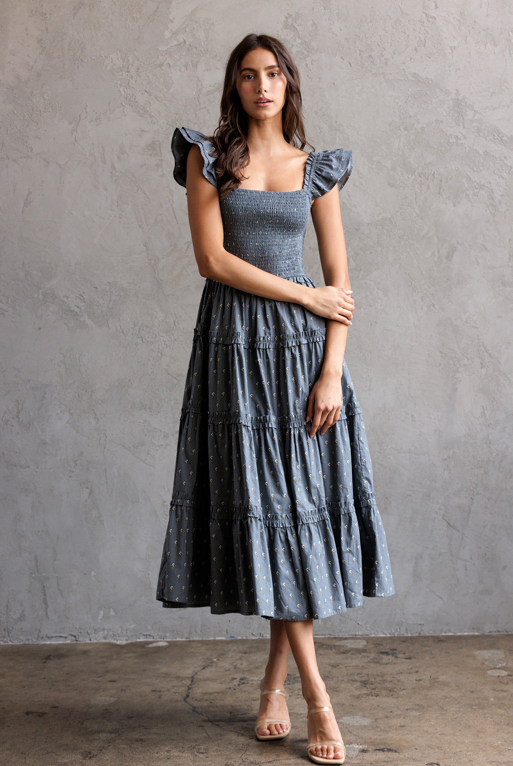 Woman wearing a blue tiered dress against a gray background