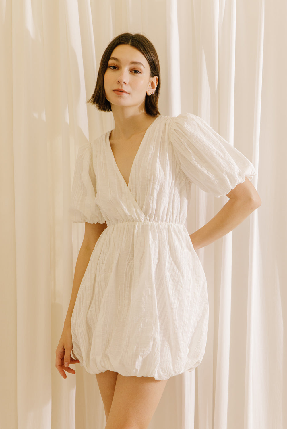 Woman wearing a white dress against a beige curtain background