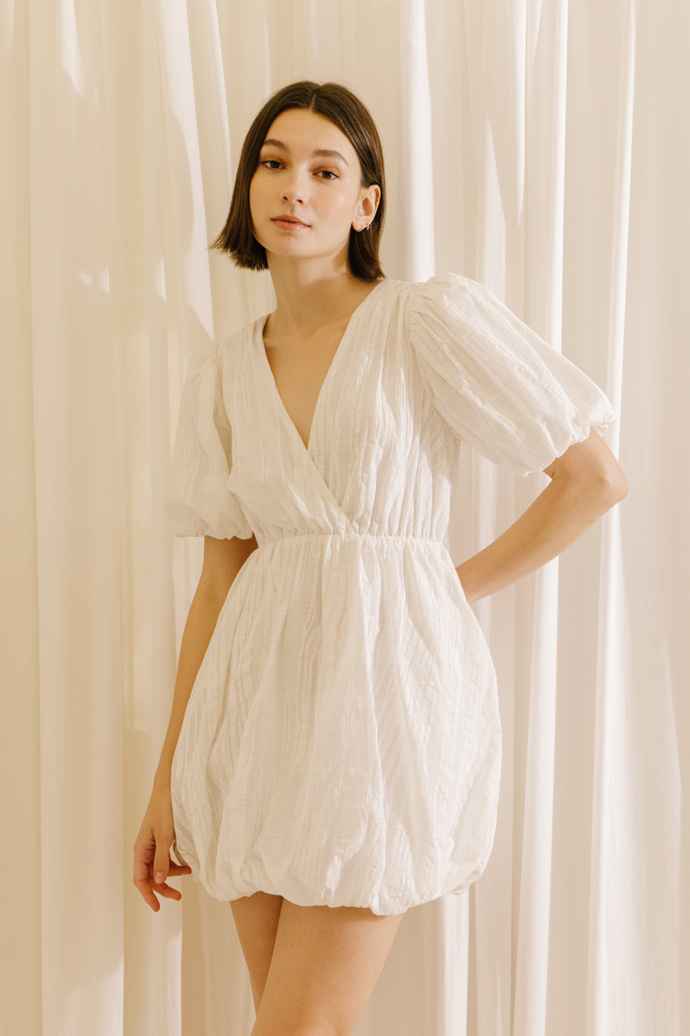 Woman wearing a white dress against a beige curtain background