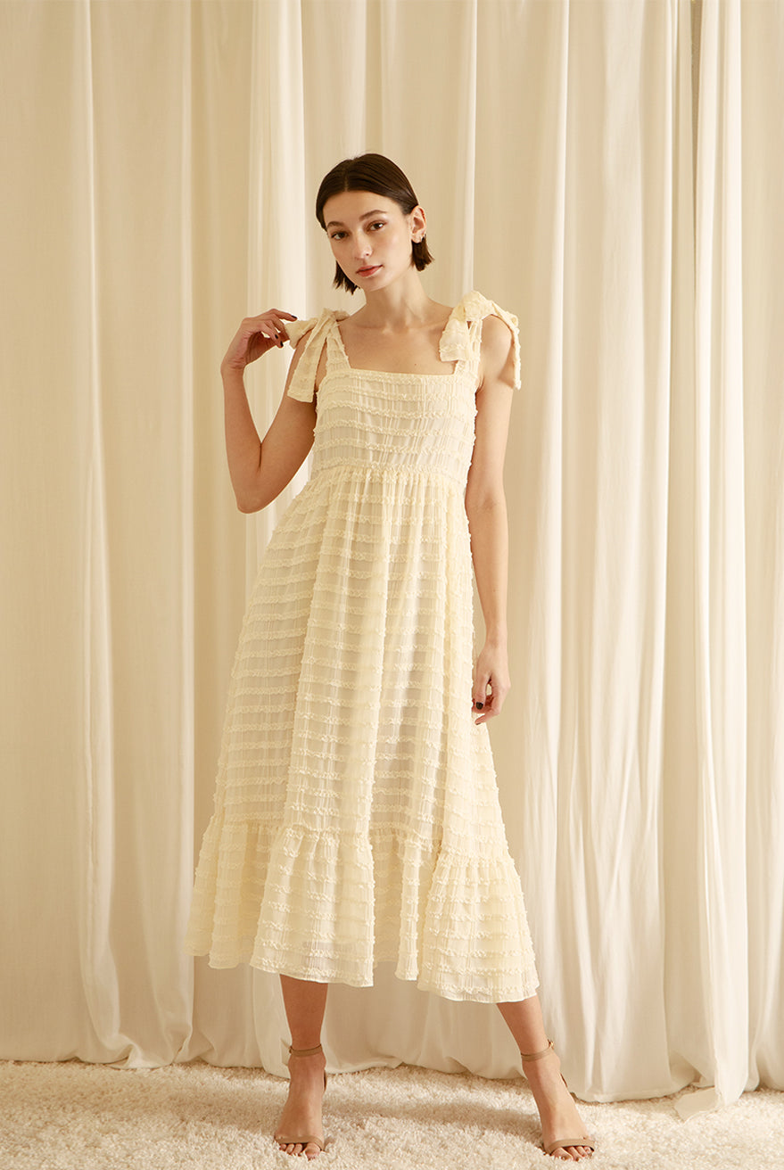 Woman wearing a cream midi dress standing in front of white curtains