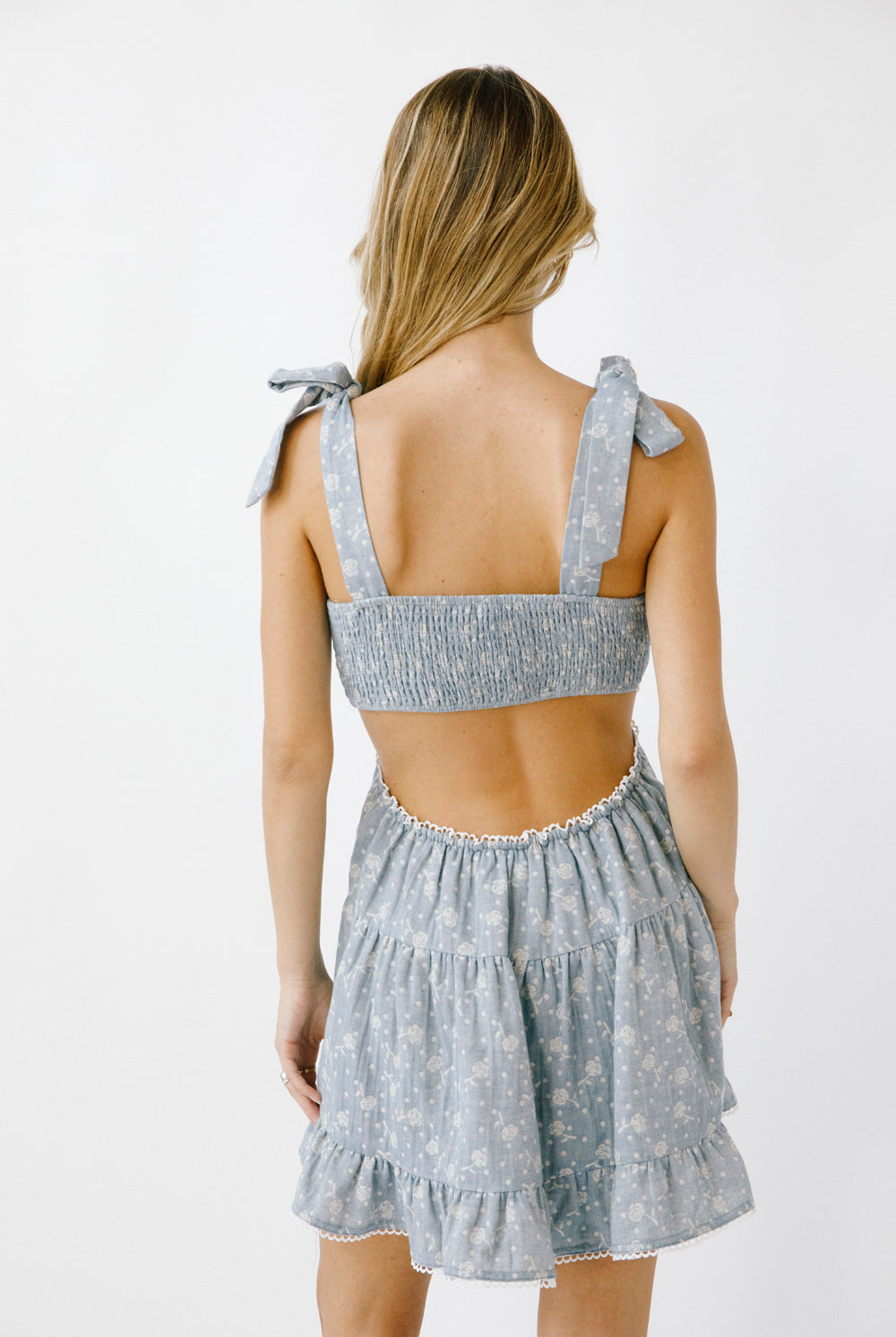 Back view of a woman wearing a blue denim floral dress against a white background