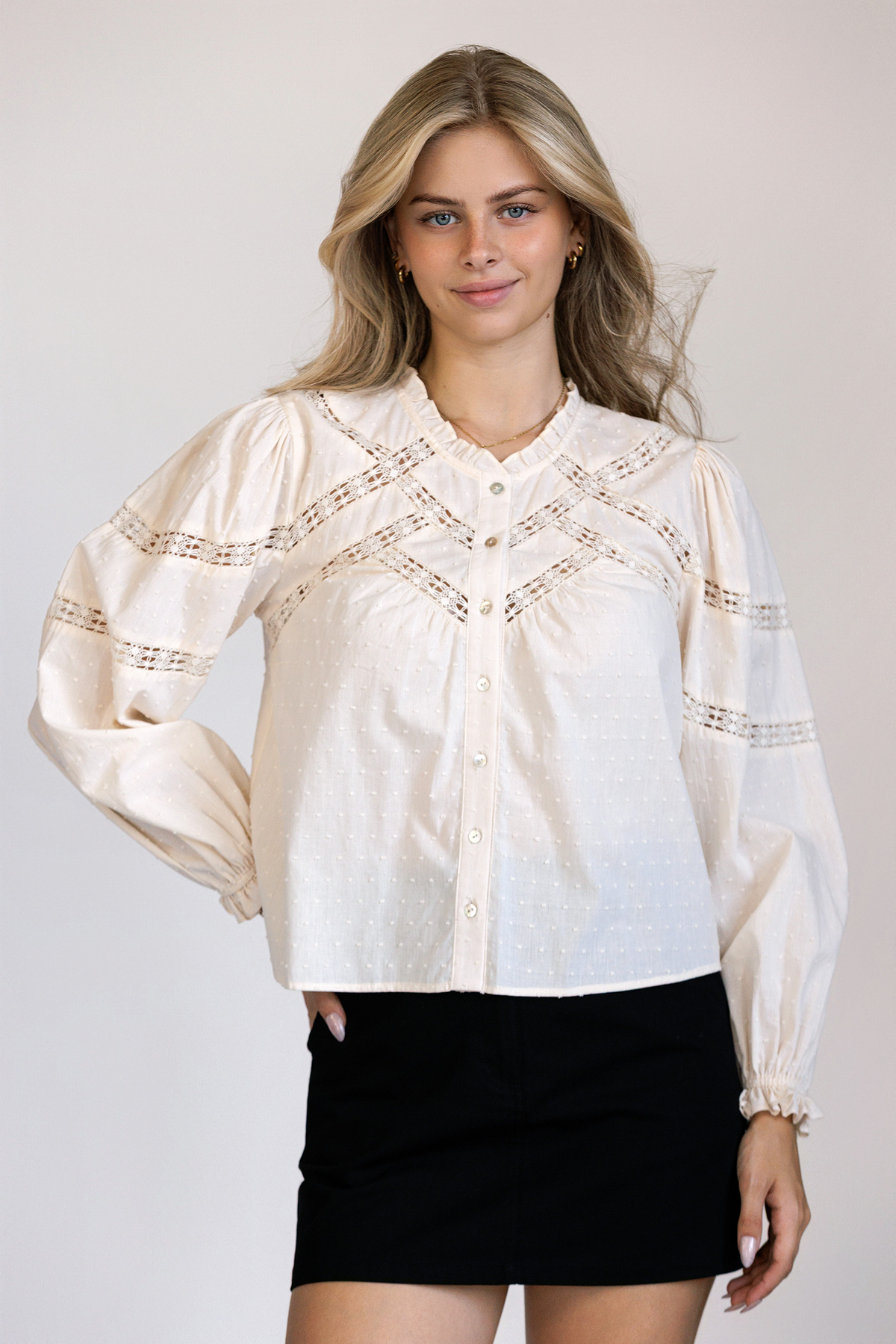 A model wearing a textured Swiss dot cotton top with lace paneling, puff sleeves, and a relaxed button-front silhouette.