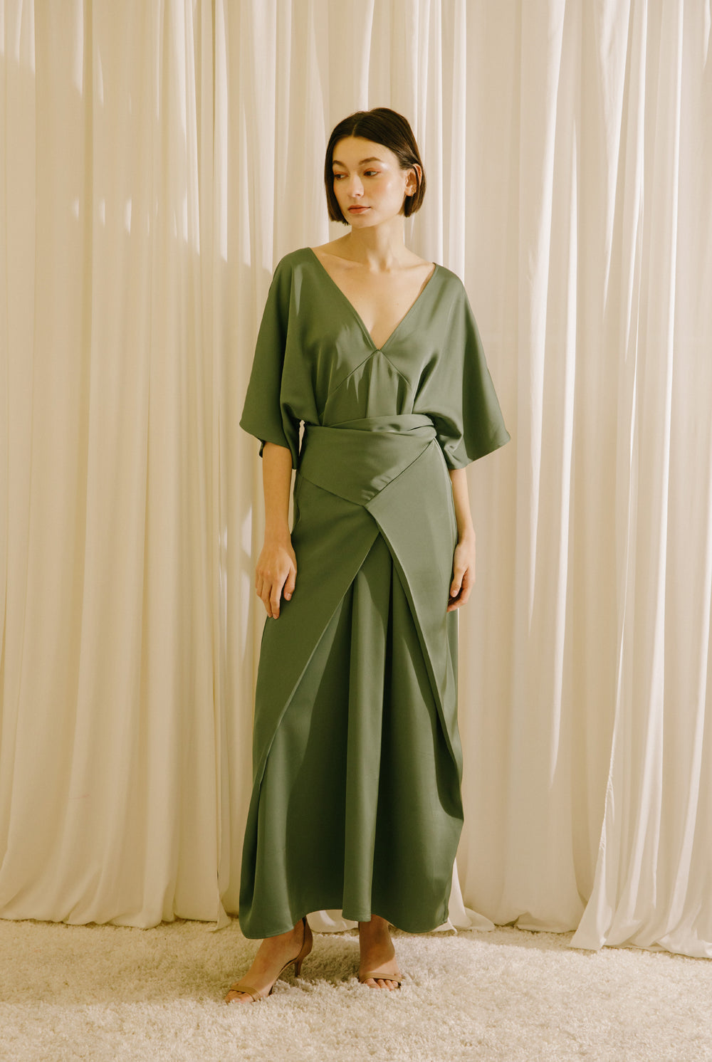 Woman wearing a green dress standing against a beige curtain backdrop
